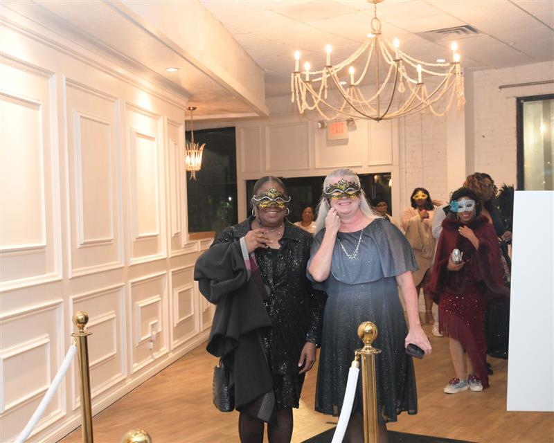 Women behind masks smiling on black carpet entrance
