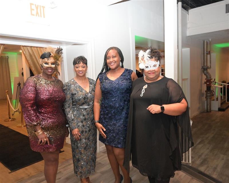 Group of four smiling women in formal attire, two wearing masks