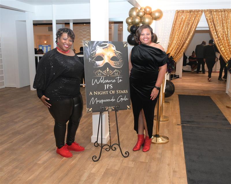 Smiling women in black with red shoes flanking the Welcome to JPS Night of Stars Gala sign